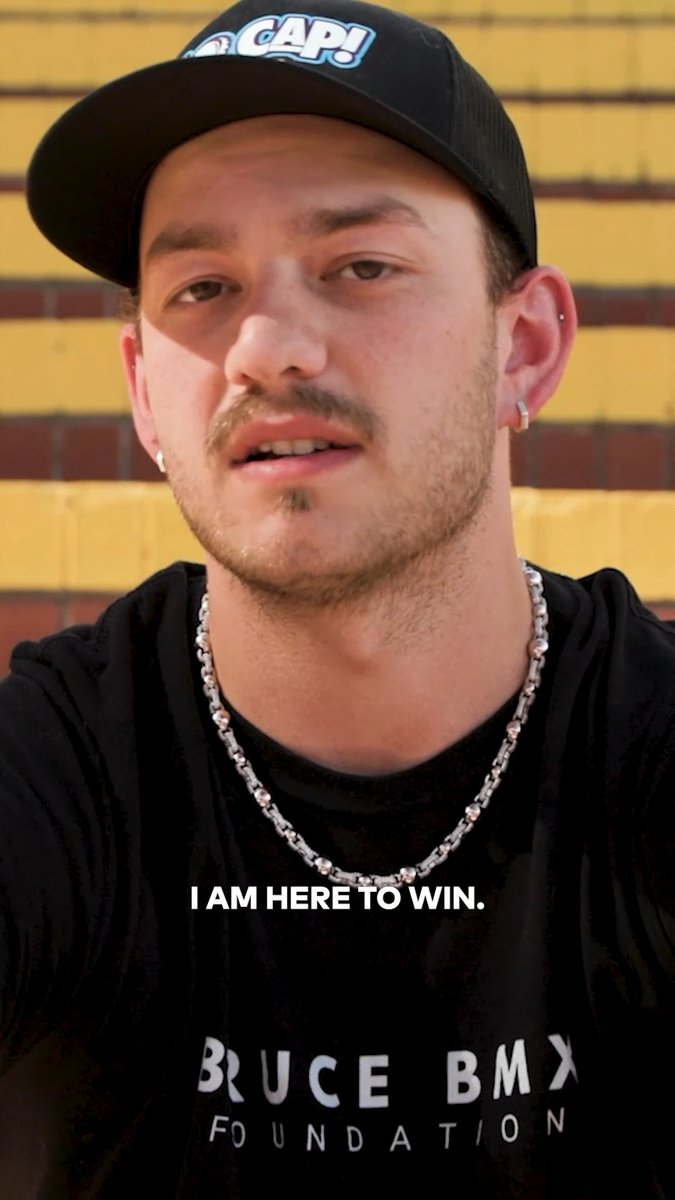 A close-up of Justin Dowell wearing a black "CAP!" cap and a Bruce BMX Foundation shirt, with the caption "I AM HERE TO WIN." overlaid on the image, reflecting the post's message about his competitive mindset heading into the Moonpay X Games League season opener against Kevin Peraza in Sacramento.