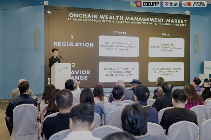 Conference photograph showing a speaker at a podium presenting on 'ONCHAIN WEALTH MANAGEMENT' with a slide highlighting J.P. Morgan's stablecoin market forecast and regulatory catalysts including the U.S. GENIUS Act.