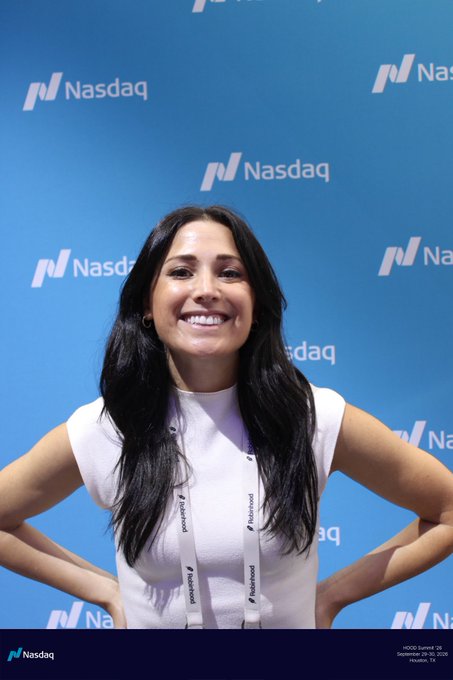 A smiling woman with long dark hair wearing a white top and a 'Haystack' lanyard, posing in front of a blue Nasdaq branded backdrop.