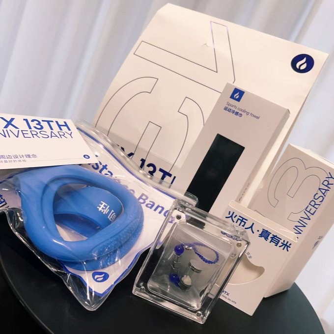 13th anniversary promotional merchandise is displayed, including a blue wristband, a keychain with blue beads, and packaging for a sports cooling towel, with text reading 'X 13TH ANNIVERSARY'.