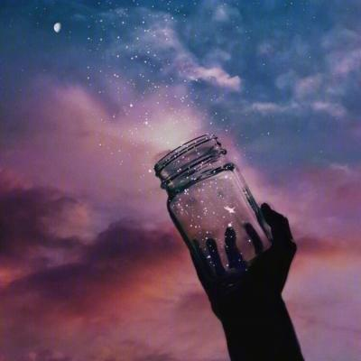 A silhouette of a hand holding a glass jar containing a galaxy and stars, set against a purple and pink sunset sky.