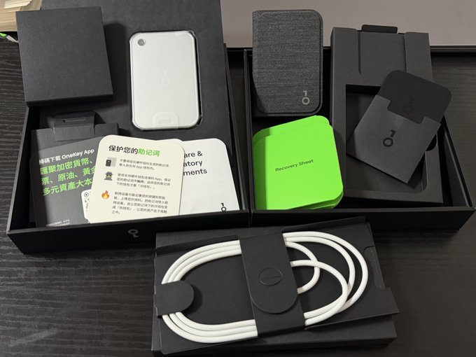 An opened black box displays a smartphone, charging cable, documentation in Chinese and English, a recovery sheet, and accessories branded with the OneKey logo.