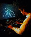 A person in silhouette plays a piano keyboard illuminated with neon colors, with a glowing 'BA' logo displayed on a screen behind them.