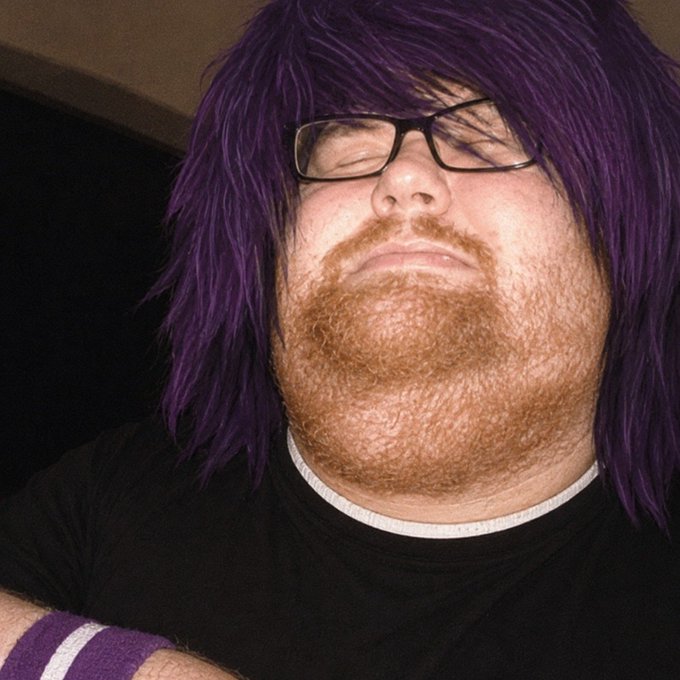 The image features a man with long purple hair wearing glasses, a black shirt, and a striped wristband. He has his eyes closed and appears to be sleeping or taking a nap. The caption of the image reads "monad is a dead chain" which could be interpreted as a reference to the monad character from the video game series "Minecraft".