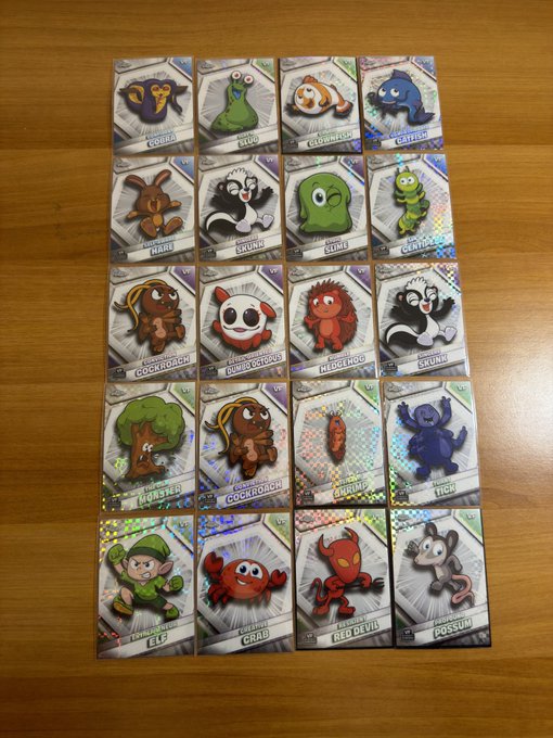 Twenty holographic trading cards featuring various cartoon creatures like monsters, crabs, and devils are arranged in a grid on a wooden surface.