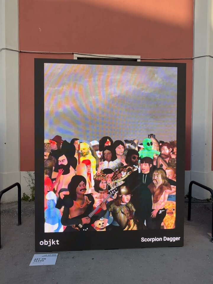 The image features a large poster or painting displayed outdoors, possibly for an art show or exhibition. The artwork depicts a group of people wearing costumes, with some individuals holding objects like a guitar and a microphone. The poster has a digital display that shows the time as "11:55". The post also mentions that it is related to the Art on Tezos screening program at @NFC Summit Lisbon Explore.