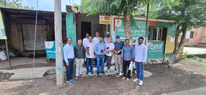 Group of men posing for a photo in front of a building with Hindi signage that includes the word 'देहात' (Dehat).