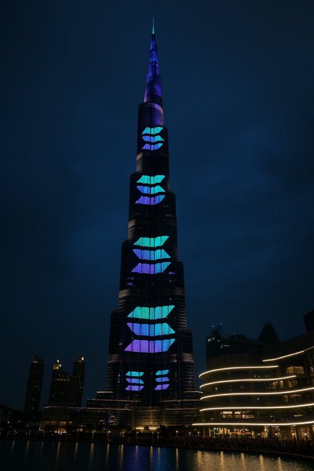 The Burj Khalifa is illuminated at night with purple and blue lip-shaped light projections on its facade.