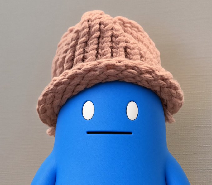 A blue cartoon character with a neutral expression wearing a knitted pink/dusty rose colored beanie.
