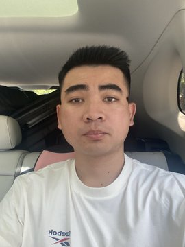 The image features a man wearing a white t-shirt with blue text that says "Kodak" on it, sitting inside a car. The man appears to be looking directly at the camera while posing for the photo.