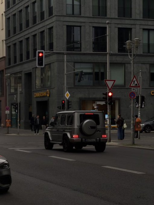 A black SUV drives through a city intersection with traffic lights and a building labeled 'COMMERZBANK' in the background.