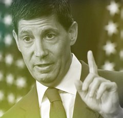 A green-tinted, close-up image of a man in a suit pointing his index finger upward.