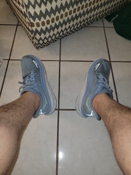 A first-person view looking down at two feet wearing blue Nike sneakers standing on a tiled floor.