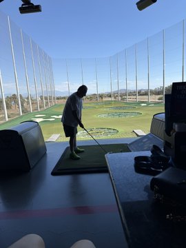 A silhouette of a person practicing their golf swing inside an indoor driving range simulator, with virtual targets displayed on a large screen.
