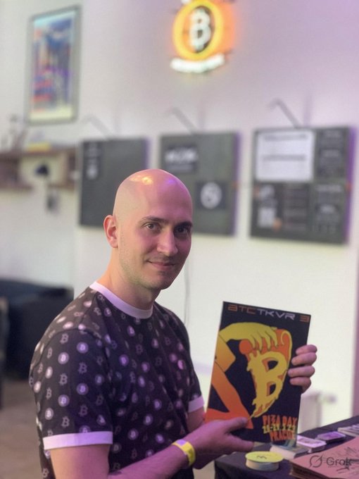 A man with a bald head holding up a book titled "btc-trava".