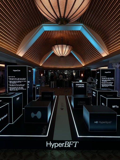 A sleek, illuminated exhibition booth for Hyperliquid (HyperBFT) featuring branded display panels showcasing its ecosystem products like HyperCore, HyperEVM, Spot, and Hyperliqud, set in a sophisticated venue with warm pendant lighting overhead.