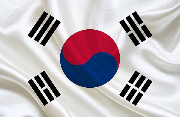 A waving fabric displaying the South Korean flag with its distinctive red and blue taegeuk symbol and four black trigrams on a white background.