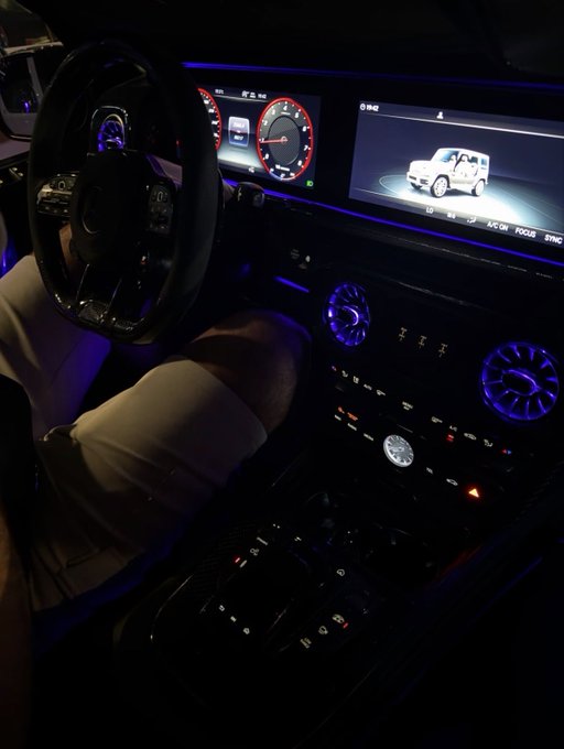 A nighttime view of a luxury vehicle's interior showcases an illuminated dashboard with blue ambient lighting, digital displays showing a Mercedes-Benz G-Class, and a multi-function steering wheel. The image's sleek, high-end aesthetic ties into the post's crypto promotion, where the modern, premium vibe complements the appeal of the "$SOL" token request.