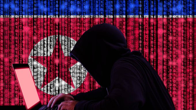 A shadowy hooded figure types on a laptop in front of a North Korean flag rendered in binary code, symbolizing the clandestine cyber operations of North Korea's Lazarus Group. The image visually reinforces the post's narrative about state-sponsored hacking and the massive $351.6M Bitget wallet breach.