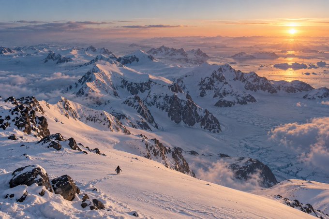 A breathtaking landscape photograph of snow-capped mountain peaks above a sea of clouds, illuminated by a golden sunset or sunrise, with a tiny figure of a hiker on a snowy ridge.