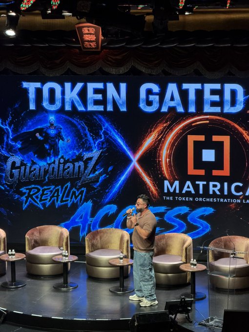 A man speaks on stage at an event with a screen reading 'TOKEN GATED ACCESS', 'GuardianZ Realm', and 'MATRICA'.