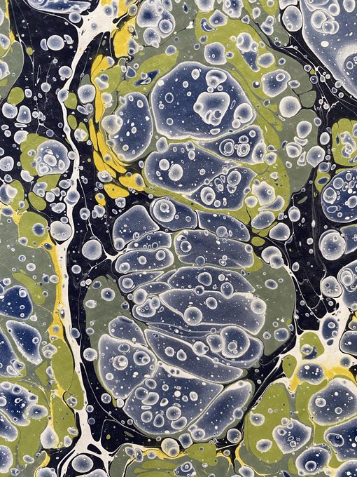An abstract marbled art piece featuring swirling olive green, navy blue, black, and yellow colors with bubble-like white circular patterns throughout.