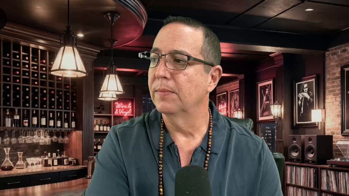 In this image, there is a man sitting at a desk with headphones on his head while he looks down at something. The background features a wine cellar or bar area filled with various bottles of wine displayed behind him. There are also multiple copies of the same bottle visible in front of the man. The man's position and focus suggest that he might be recording a podcast, video or live stream about tokenization or a particular topic related to it, as there is a laptop open before him on the desk. Additionally, there is a post at the bottom with information about $500T in tokenization and XRP today.