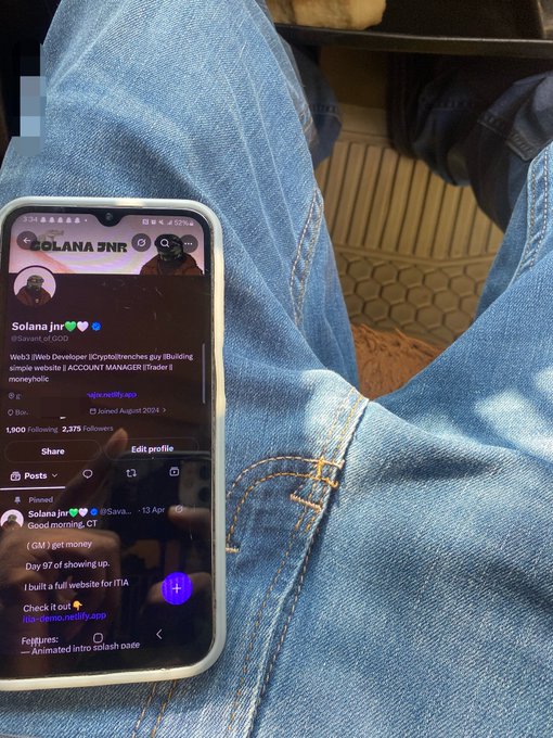 A smartphone resting on someone's lap displays the X (formerly Twitter) profile of 'Solana Jn' (@solanajr), a Web3 developer and crypto enthusiast with 1,900 following.