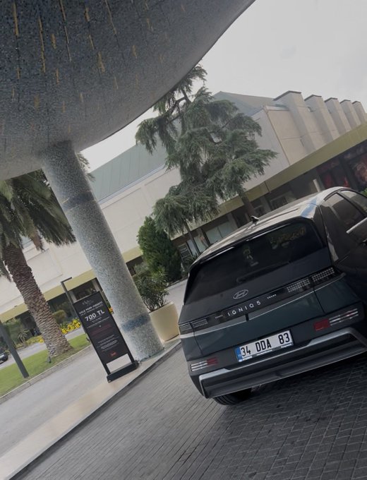A dark gray Hyundai Ioniq 6 with license plate "34 DDA 83" is parked beneath a modern canopy at what appears to be a dealership, complementing the "GM" post by showcasing an electric vehicle from Hyundai's expanding EV lineup.