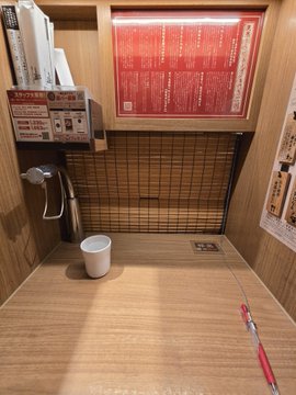 A traditional Japanese-style indoor foot bath or small tub with wooden surroundings, a small white bucket, and a bamboo blind, with a red menu or price list mounted on the wall above.