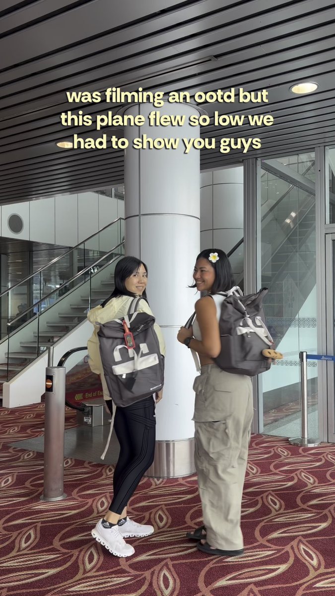 Two young women with backpacks pose for a photo in what appears to be an airport terminal, with text overlay reading 'was filming an ootd but this plane flew so low we had to show you guys'.
