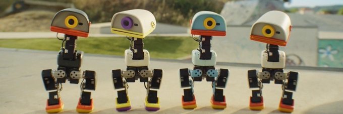 Four small humanoid robots with colorful, rounded heads and exposed mechanical joints stand side by side outdoors, each featuring a distinct eye color or design. The image visually reflects the post's mention of Pollen Robotics, showcasing the playful, identity-driven aesthetic of MicroDuck, a project that leverages this robotics ecosystem to stand out in an early-stage market.