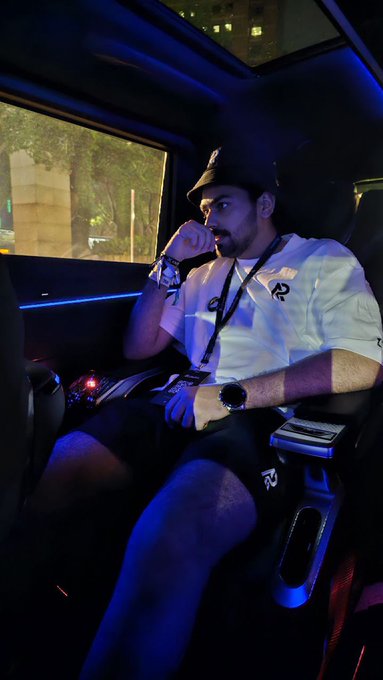 A man wearing a black cap and white esports jersey with a number "22" sitting in a gaming chair with blue LED lighting in the background.