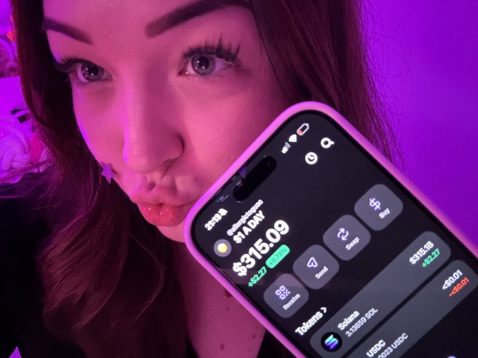 A close-up selfie of a person under pink lighting holding a smartphone displaying a crypto trading app with '$1ADY $315.09 +$2.27' and 'Solana 3.139693 SOL' visible on the screen.