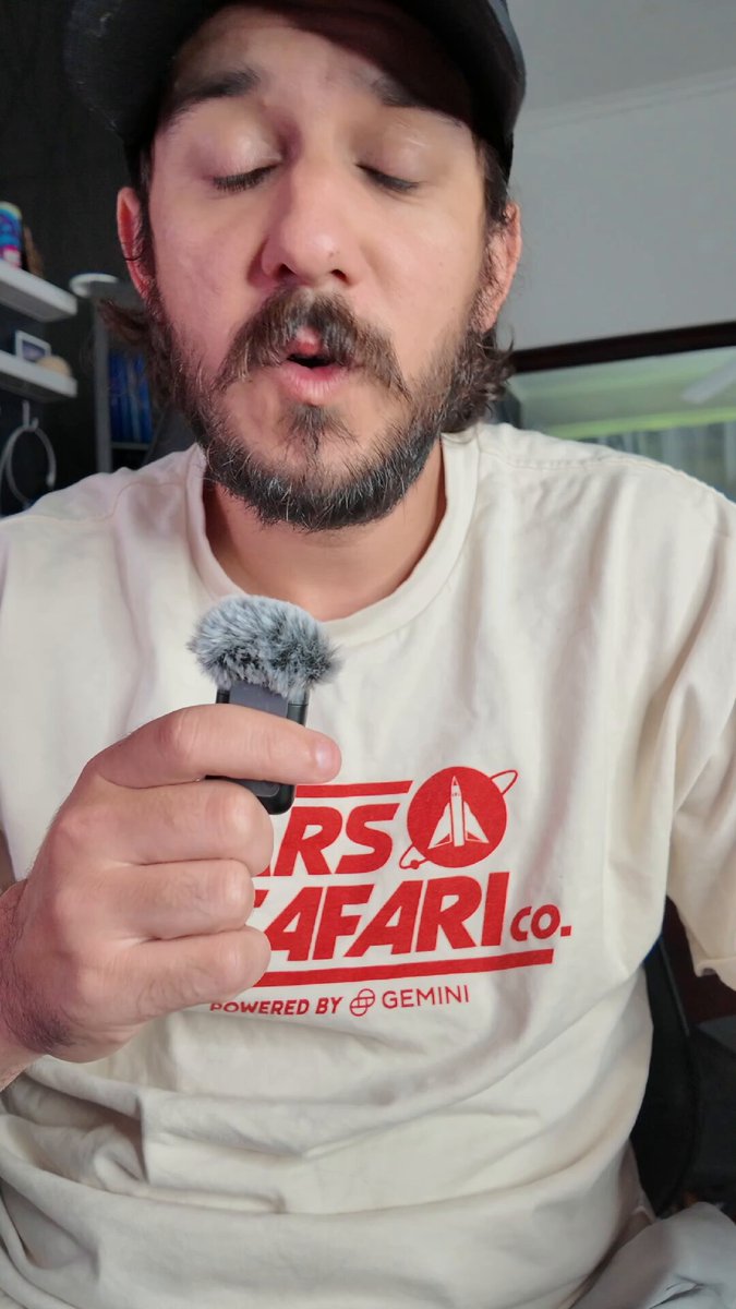 A man with a beard holding a microphone and wearing an "RTS & SAFFARI" t-shirt while recording something.