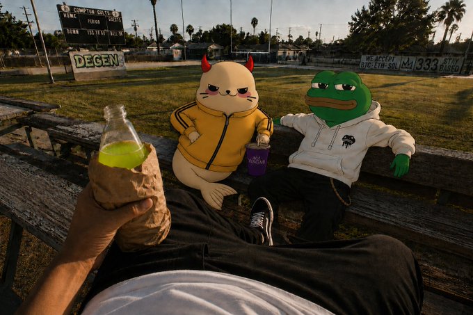 Seals and Plague, depicted as a seal in a yellow hoodie and Pepe the Frog in a white hoodie, relax on a park bench while a person holds a bottle wrapped in brown paper, with a "Compton Soldiers" scoreboard and "DEGEN" sign visible in the background.