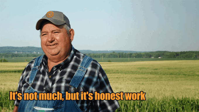 A man in overalls and a plaid shirt stands in a field with the caption 'It's not much, but it's honest work'.
