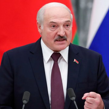 A photograph of Belarusian President Alexander Lukashenko, an older man with a mustache wearing a dark suit and tie, speaking at a podium.