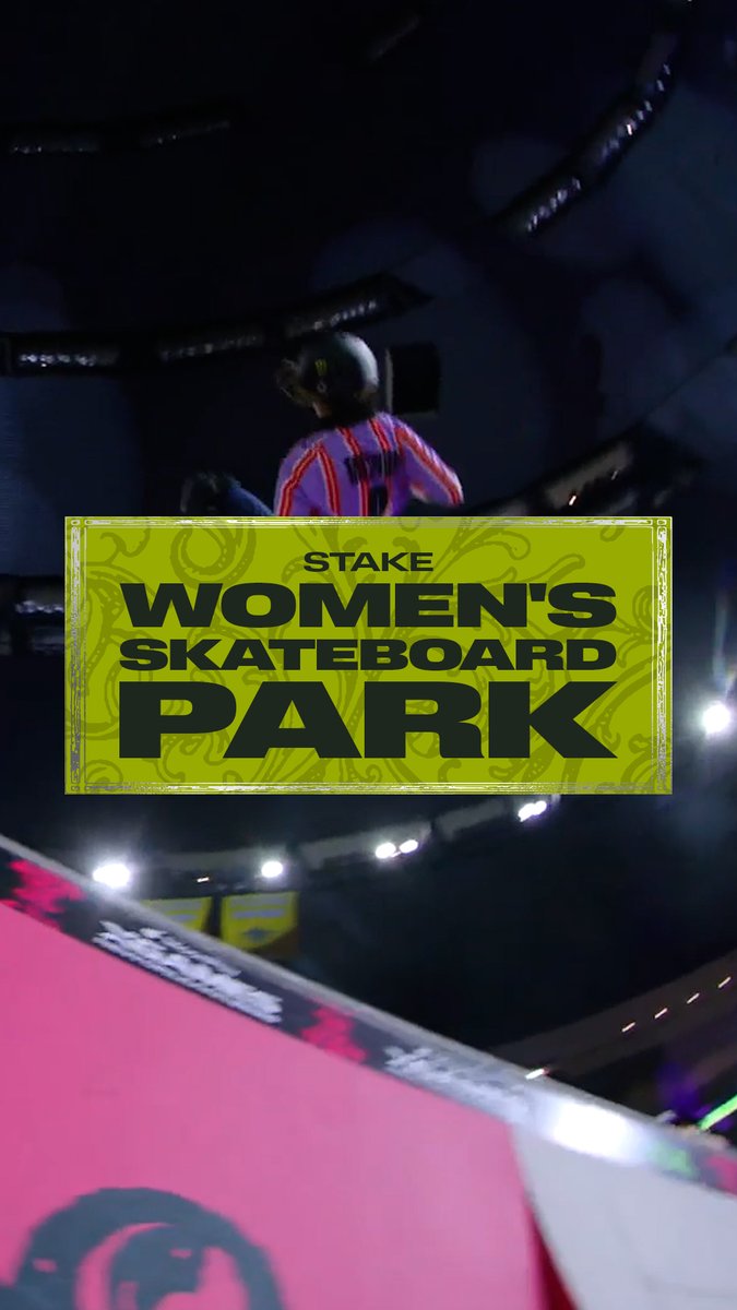 A low-angle shot at the "STAKE WOMEN'S SKATEBOARD PARK" event, showing a skateboarder in a red and blue striped jersey and helmet at the top of a halfpipe ramp.