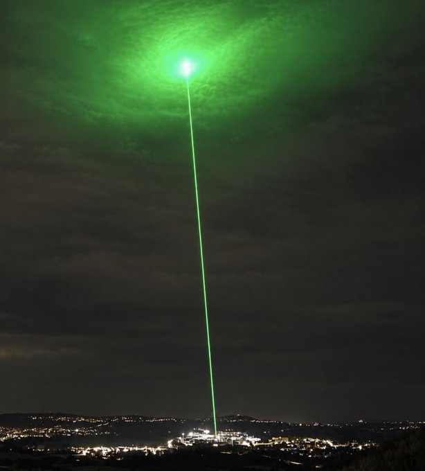A vibrant green laser beam shoots into the night sky above a city, symbolizing the hopeful "to the moon" rocket trajectory the post uses to promise a massive crypto bull run. The lone green streak rising against dark clouds visually echoes the message that holding now will lead to retirement gains.