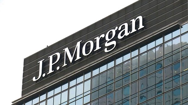 The image shows the "J.P.Morgan" logo displayed on the exterior of a modern glass building. This visually represents the banking giant referenced in the post, which discusses JPMorgan's commentary on digital assets becoming central to the US financial system.