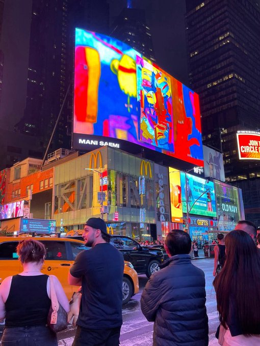 A nighttime scene in Times Square features a large digital billboard displaying colorful abstract artwork credited to "MANI SAEMI," with McDonald's and Old Navy advertisements visible below and pedestrians watching from the street.
