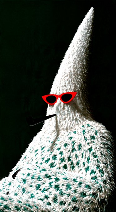 A whimsical photograph of a fluffy white and green knitted wizard or gnome figure wearing red cat-eye sunglasses and smoking a black pipe against a dark background.