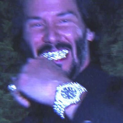 A close-up photo of a man with a mustache grinning and showing off a large diamond-encrusted watch and grillz, with a dark outdoor background.