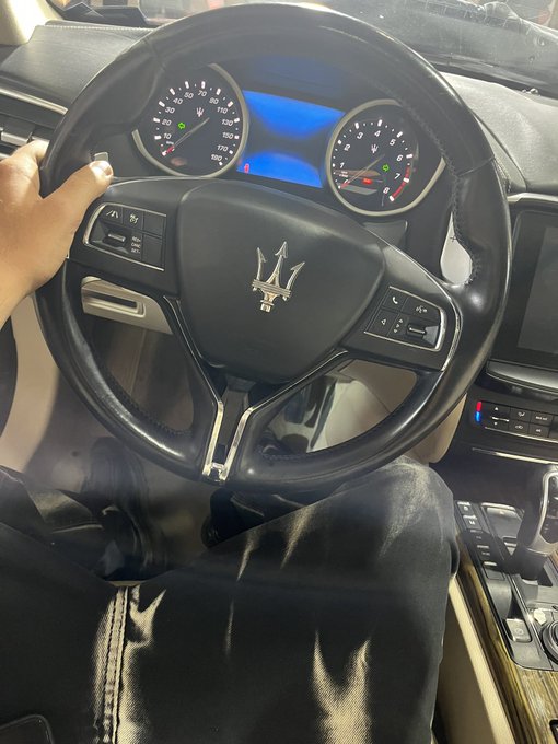 A view from the driver's seat of a Maserati, showing the steering wheel with the trident logo and the dashboard instrument cluster.