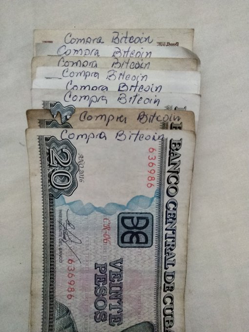 Several Cuban 20 peso bills are folded with "Compra Bitcoin" (Buy Bitcoin) handwritten on each, demonstrating a creative grassroots effort to promote Bitcoin adoption in Cuba by repurposing official currency as on-the-spot purchase notes at local businesses.