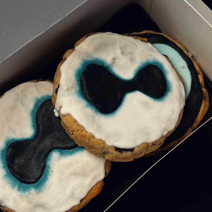 The image features a box of cookies with blue icing, each adorned with black bow eyes. The cookies are arranged neatly inside the white box, creating an appealing visual presentation. The text "my gf knows about my Hyperliquid addiction so she made my bday cake match" suggests that these cookies were specifically created for someone who is fond of consuming sugary treats and has a sweet tooth. This unique design choice adds a personal touch to the gift, making it more special and memorable for the recipient.