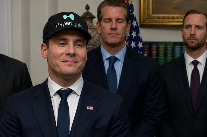A man in a suit wearing a black 'Hyperliquid' branded cap stands in front of others near an American flag.