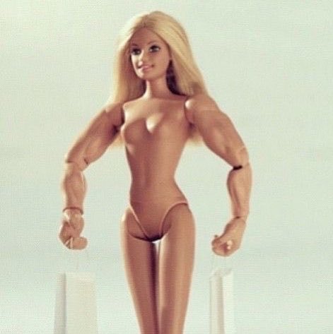 A blonde doll with an exaggerated muscular body, featuring a typical Barbie face atop a bodybuilder physique, standing against a white background.