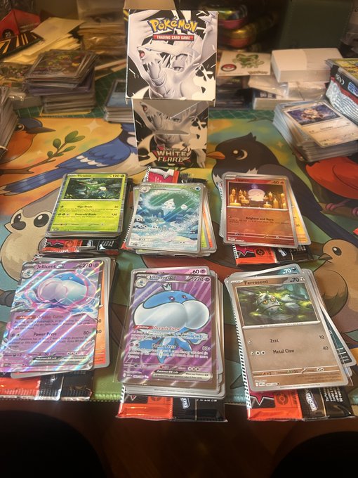A collection of Pokémon TCG cards displayed on a table with character artwork, including a White Flare booster box and various cards like Venusaur, Altaria, Volcarona, Balbasaur, and Ferroseed.